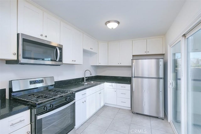 kitchen with white cabinets, appliances with stainless steel finishes, dark stone counters, sink, and light tile patterned floors