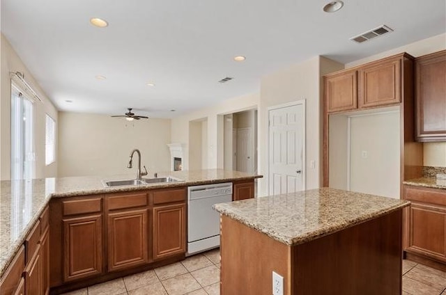 kitchen with a center island with sink, dishwasher, light stone counters, and sink