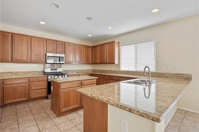 kitchen with kitchen peninsula, light stone counters, stainless steel appliances, sink, and a kitchen island