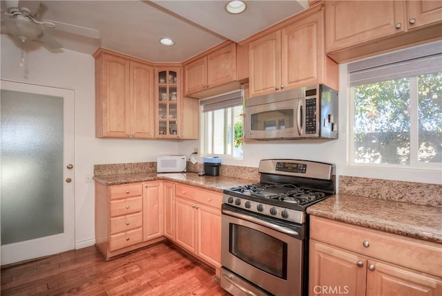 kitchen featuring light stone countertops, stainless steel appliances, ceiling fan, light brown cabinets, and light hardwood / wood-style flooring