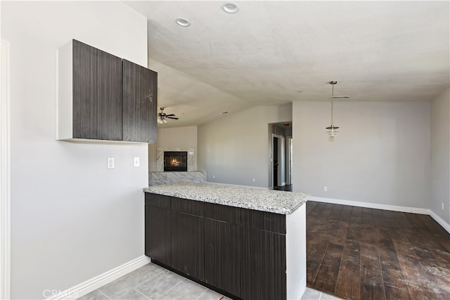 kitchen with lofted ceiling, decorative light fixtures, light hardwood / wood-style floors, light stone counters, and dark brown cabinetry