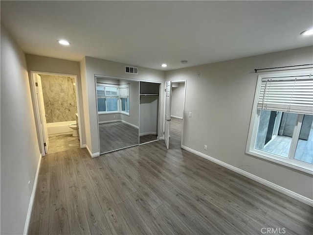 unfurnished bedroom featuring hardwood / wood-style floors, ensuite bathroom, and a closet