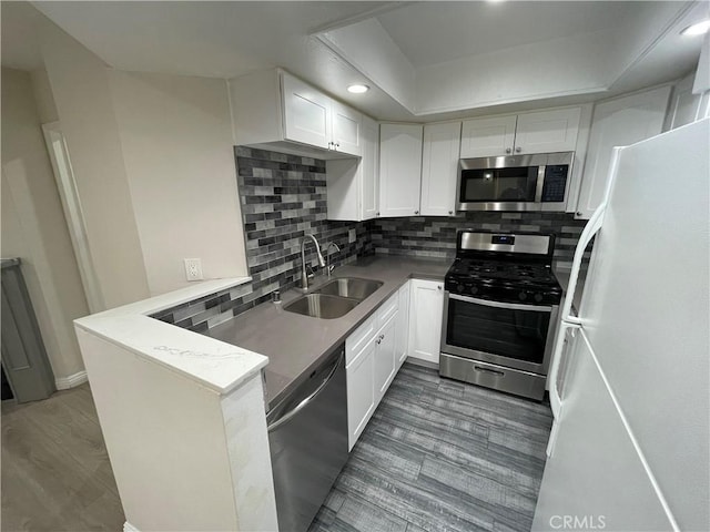 kitchen with kitchen peninsula, appliances with stainless steel finishes, tasteful backsplash, sink, and white cabinetry