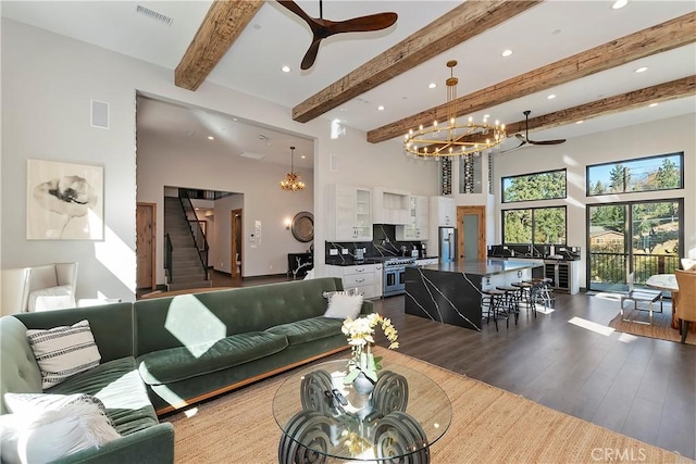 living room with beamed ceiling, a towering ceiling, hardwood / wood-style flooring, and ceiling fan with notable chandelier