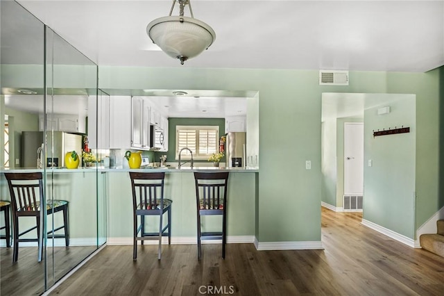 kitchen featuring kitchen peninsula, appliances with stainless steel finishes, a breakfast bar, wood-type flooring, and white cabinets