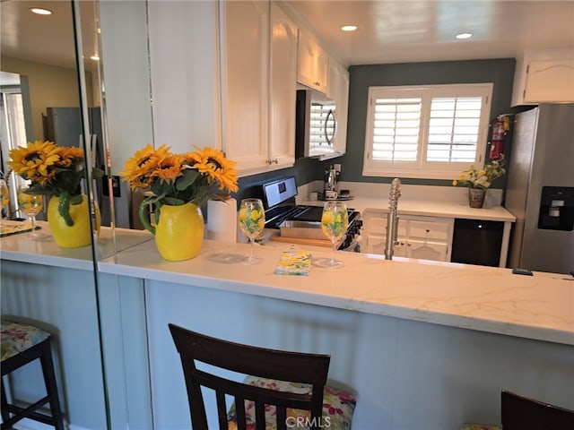 kitchen featuring light stone countertops, appliances with stainless steel finishes, a breakfast bar, and white cabinetry