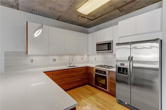 kitchen featuring backsplash, stainless steel appliances, sink, white cabinets, and light hardwood / wood-style floors