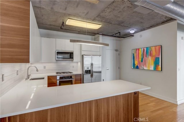 kitchen featuring white cabinetry, sink, kitchen peninsula, appliances with stainless steel finishes, and light wood-type flooring