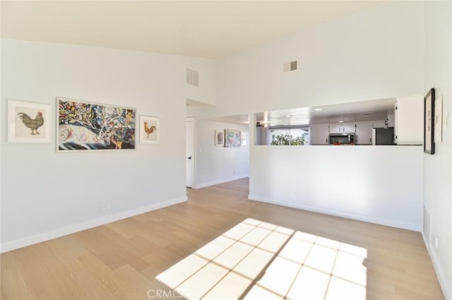 spare room with a towering ceiling and light wood-type flooring