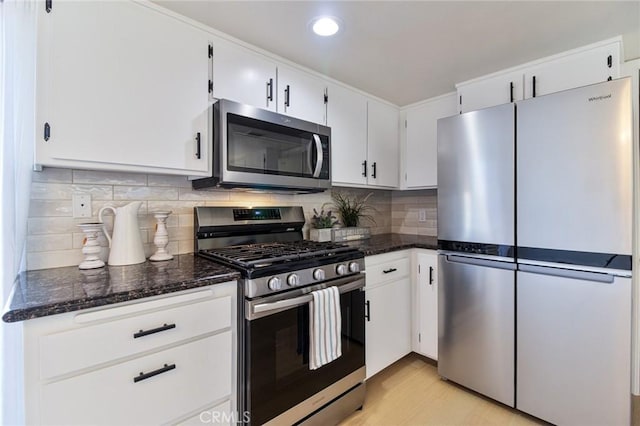 kitchen featuring dark stone counters, white cabinets, decorative backsplash, appliances with stainless steel finishes, and light hardwood / wood-style floors