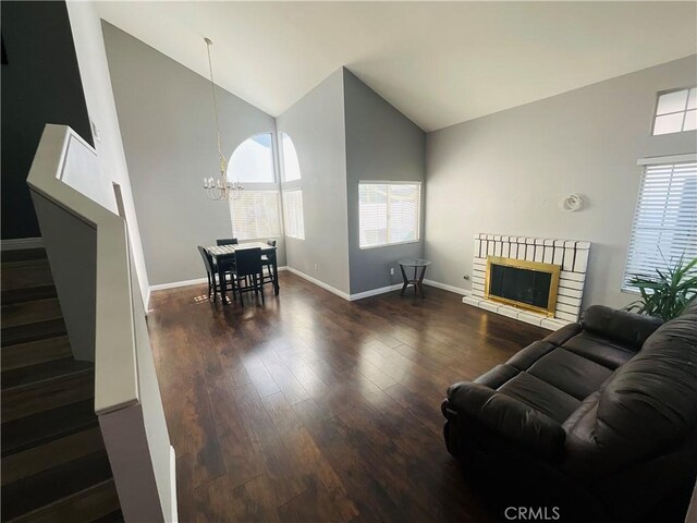 living room with dark hardwood / wood-style flooring, an inviting chandelier, high vaulted ceiling, and a healthy amount of sunlight