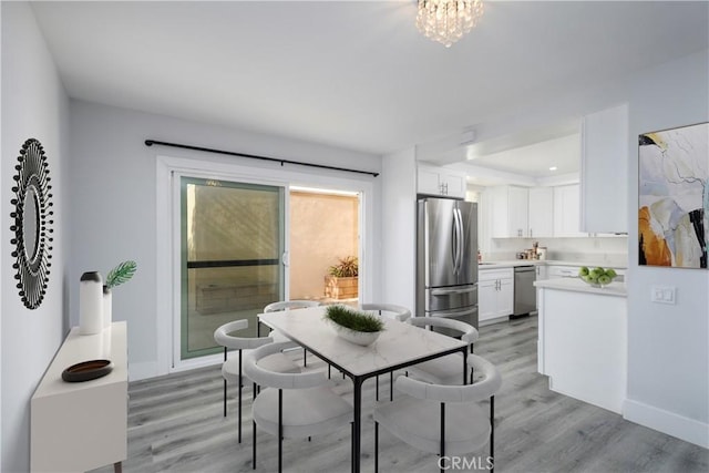 dining space featuring light wood-style flooring, baseboards, and an inviting chandelier