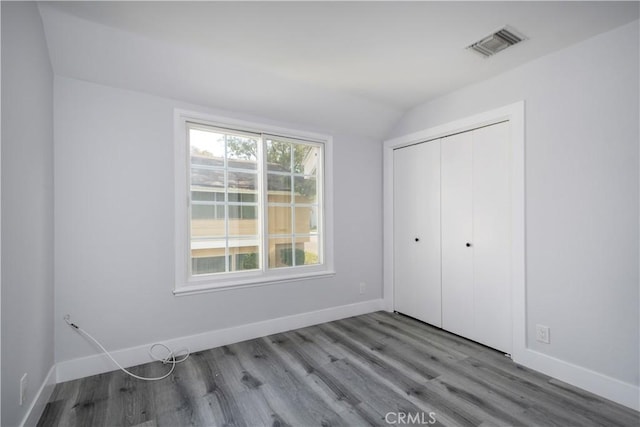 unfurnished bedroom featuring visible vents, baseboards, vaulted ceiling, a closet, and light wood-type flooring