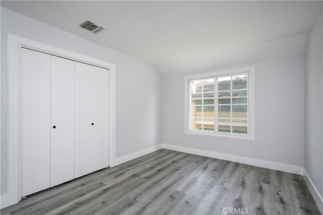 unfurnished bedroom with lofted ceiling, visible vents, baseboards, a closet, and light wood finished floors