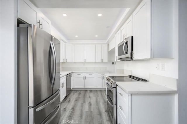 kitchen with light stone counters, light wood finished floors, stainless steel appliances, recessed lighting, and white cabinetry