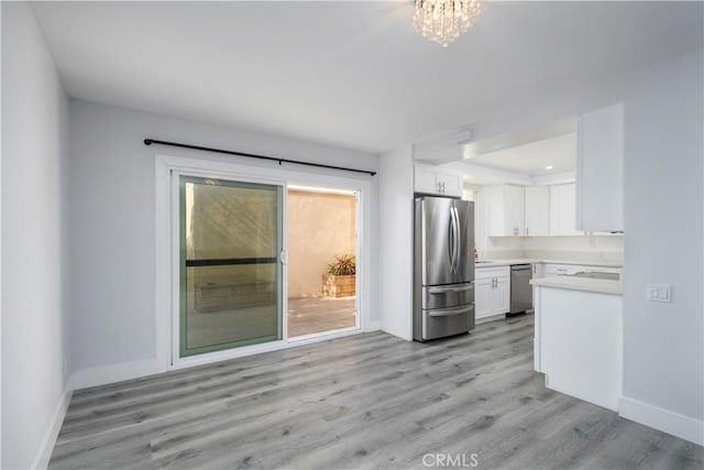 kitchen featuring light wood finished floors, light countertops, appliances with stainless steel finishes, white cabinets, and baseboards