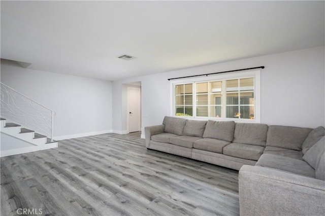 unfurnished living room featuring light wood-type flooring, visible vents, baseboards, and stairs