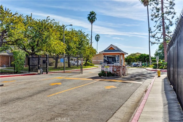 view of road featuring curbs, street lighting, a gated entry, and sidewalks