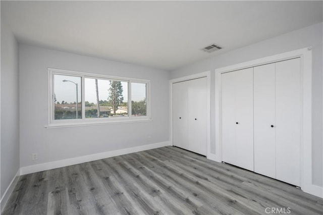 unfurnished bedroom with baseboards, visible vents, light wood-style flooring, and multiple closets