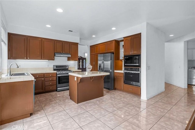 kitchen with stainless steel appliances, sink, light tile patterned floors, a center island, and a breakfast bar area