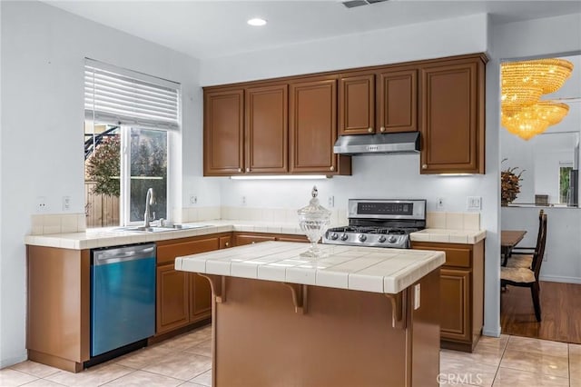 kitchen featuring tile countertops, sink, light tile patterned floors, a kitchen island, and stainless steel appliances