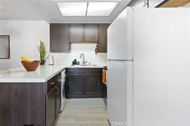 kitchen featuring dark brown cabinetry, sink, white refrigerator, washer / dryer, and light wood-type flooring