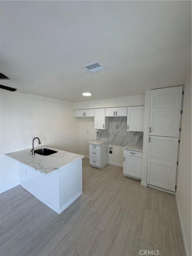 kitchen featuring kitchen peninsula, backsplash, sink, white cabinets, and light hardwood / wood-style floors