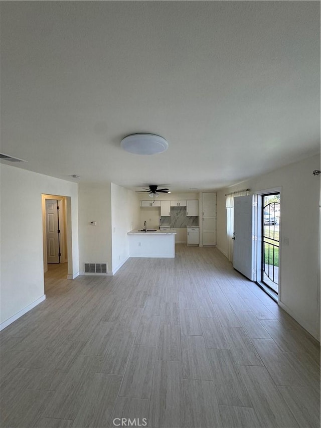 unfurnished living room with ceiling fan, light wood-type flooring, and sink