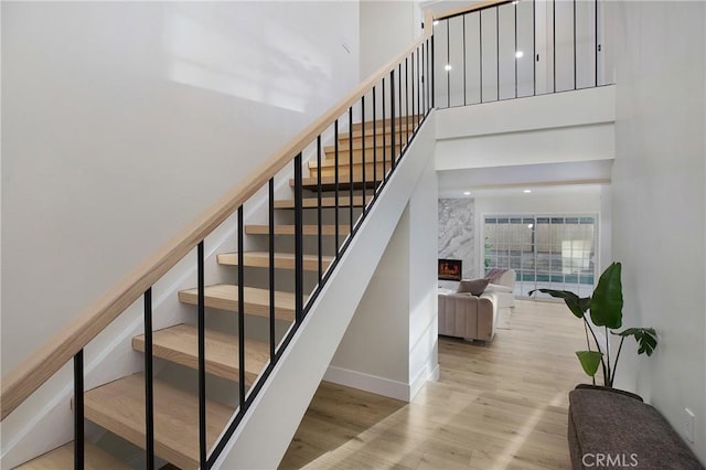 stairs with wood-type flooring, a fireplace, and a towering ceiling