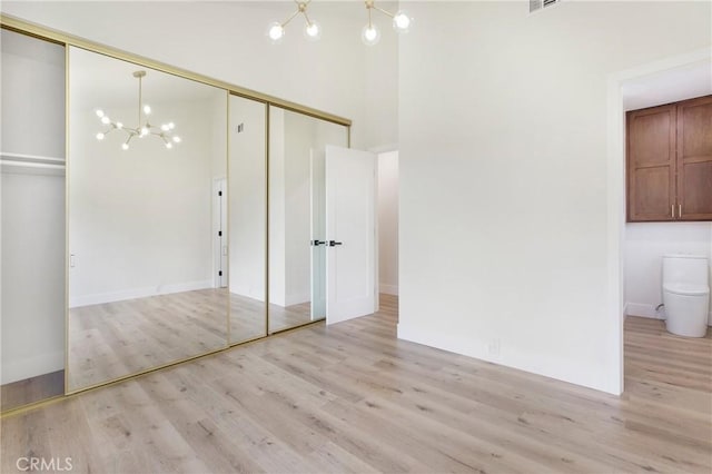 unfurnished bedroom featuring an inviting chandelier, a high ceiling, connected bathroom, light hardwood / wood-style floors, and a closet