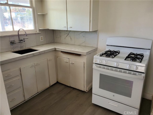 kitchen featuring decorative backsplash, gas range gas stove, sink, white cabinets, and tile counters