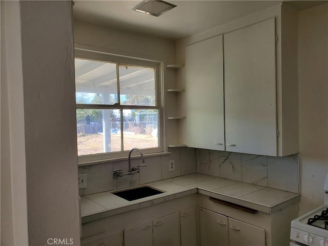 kitchen featuring white cabinetry, white gas stove, tile counters, sink, and tasteful backsplash