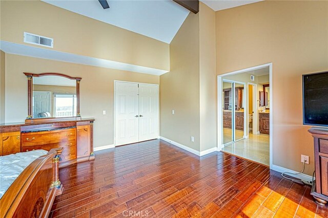 bedroom featuring connected bathroom, hardwood / wood-style flooring, high vaulted ceiling, and beamed ceiling