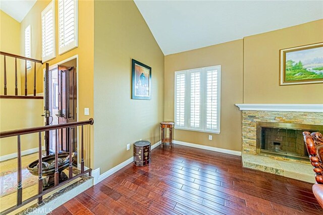 living room featuring vaulted ceiling, a stone fireplace, and dark wood-type flooring