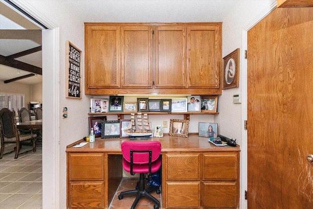 office area with light tile patterned floors, built in desk, and beam ceiling