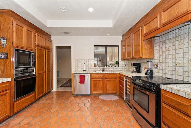 kitchen with light tile patterned floors, a raised ceiling, backsplash, black appliances, and sink