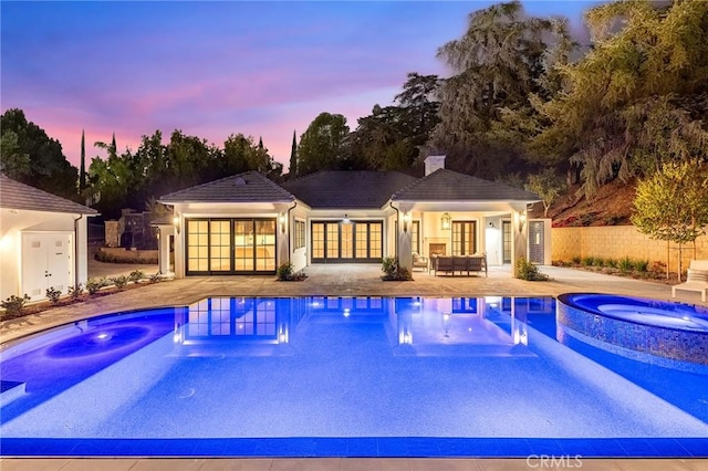 pool at dusk featuring a patio area and an in ground hot tub