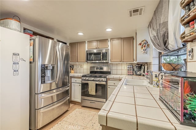 kitchen featuring sink, stainless steel appliances, tasteful backsplash, tile counters, and light hardwood / wood-style floors