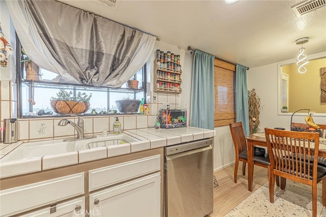 kitchen featuring sink, light hardwood / wood-style flooring, dishwasher, white cabinetry, and tile countertops