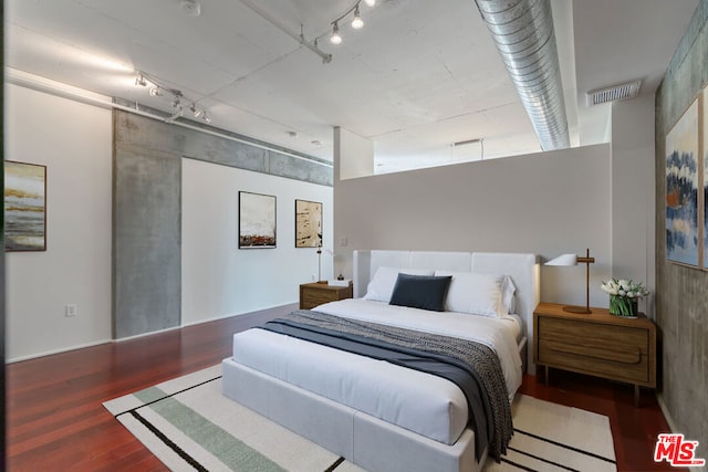 bedroom with dark hardwood / wood-style flooring and track lighting