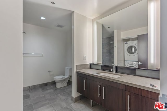 bathroom with tile patterned flooring, vanity, stacked washer and clothes dryer, and toilet