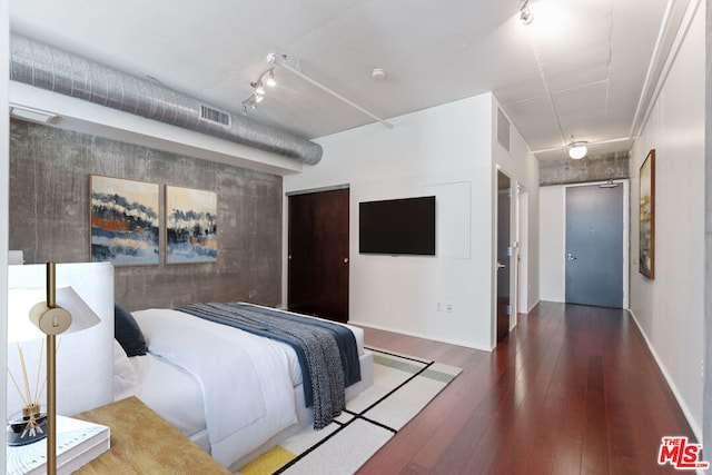 bedroom with dark hardwood / wood-style flooring and track lighting