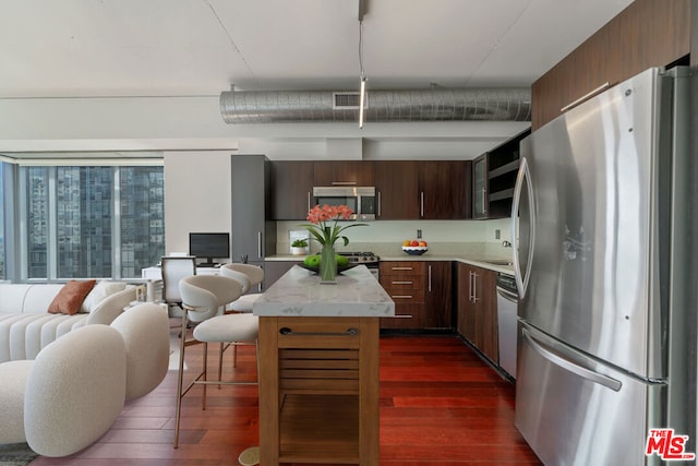 kitchen with appliances with stainless steel finishes, dark brown cabinetry, dark hardwood / wood-style floors, and a kitchen island