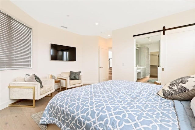 bedroom featuring a barn door, light hardwood / wood-style flooring, and ensuite bath