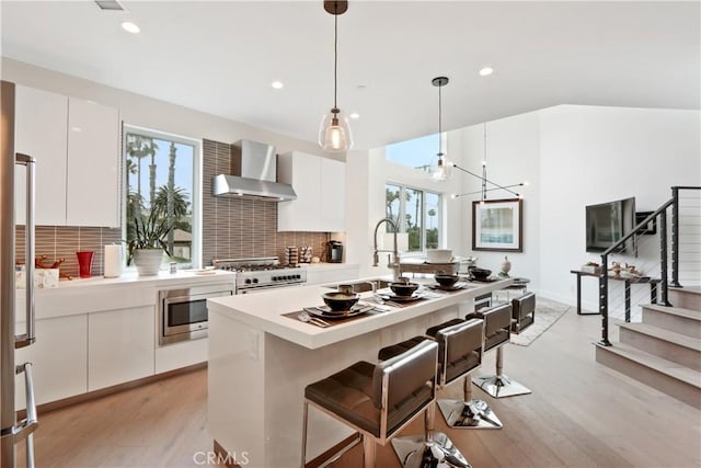 kitchen featuring white cabinets, wall chimney exhaust hood, plenty of natural light, and decorative light fixtures