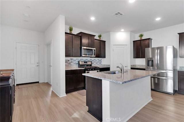 kitchen featuring light stone countertops, appliances with stainless steel finishes, light wood-type flooring, sink, and an island with sink