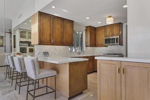 kitchen with backsplash, a kitchen breakfast bar, sink, ceiling fan, and kitchen peninsula