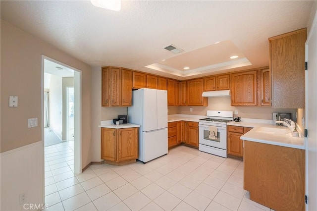 kitchen with a raised ceiling, sink, light tile patterned floors, and white appliances