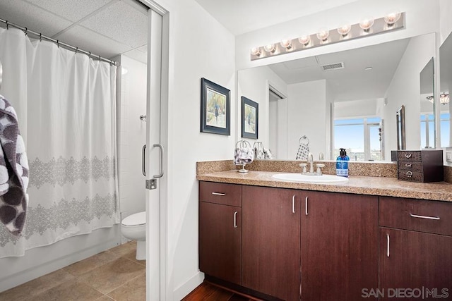 full bathroom with a paneled ceiling, vanity, shower / bath combination with curtain, tile patterned flooring, and toilet