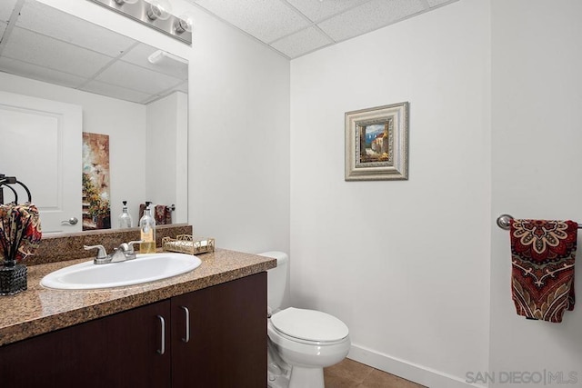 bathroom with toilet, vanity, tile patterned floors, and a drop ceiling